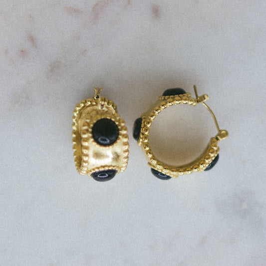 Gold hoop earrings with black stones on a marble surface