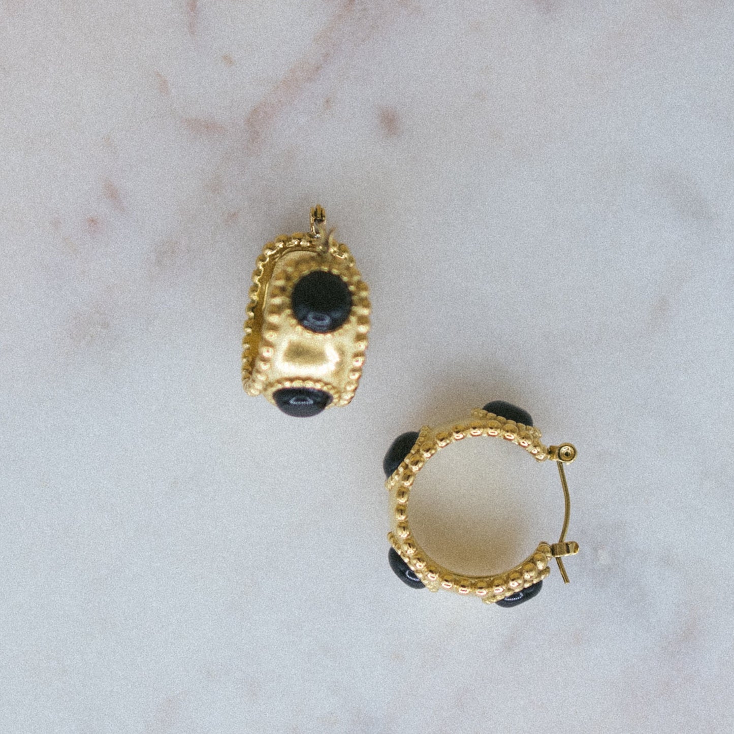 Gold hoop earrings with black gemstones on a marble surface