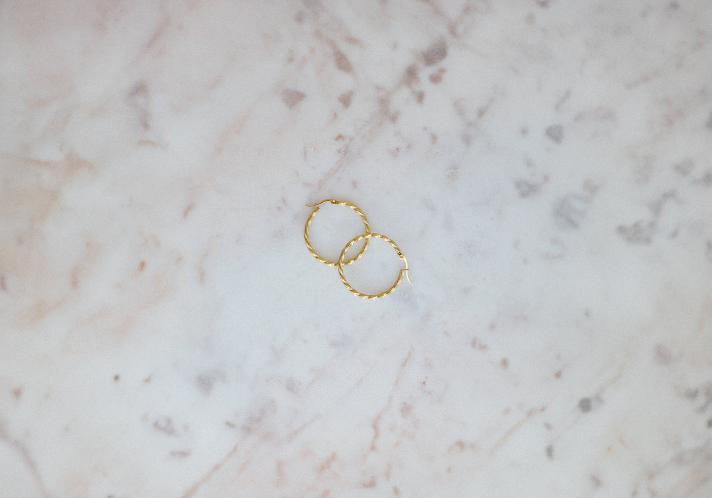 Everyday Twist Hoop Earrings. Two gold rings on a marble surface