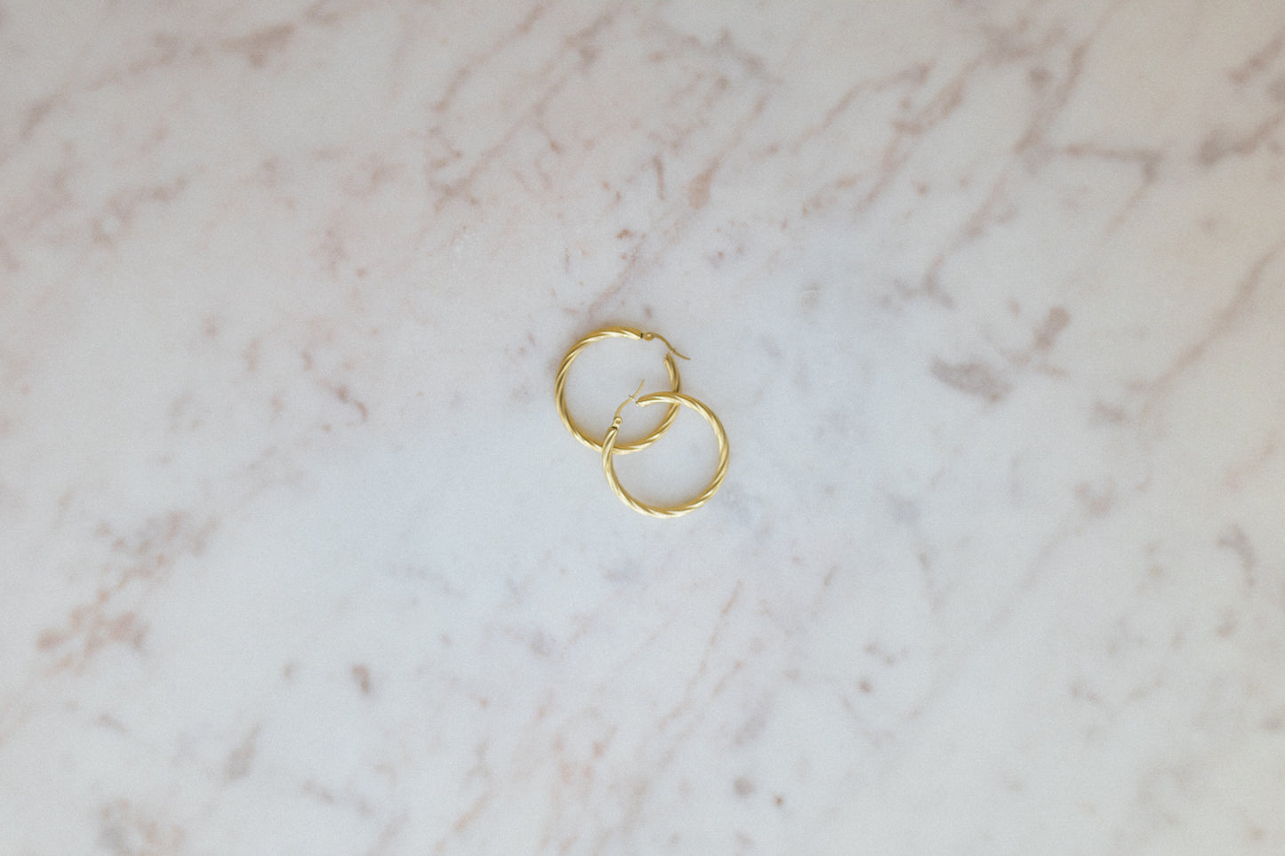 Everyday Wave Hoop Earrings. Gold hoop earrings on a marble surface