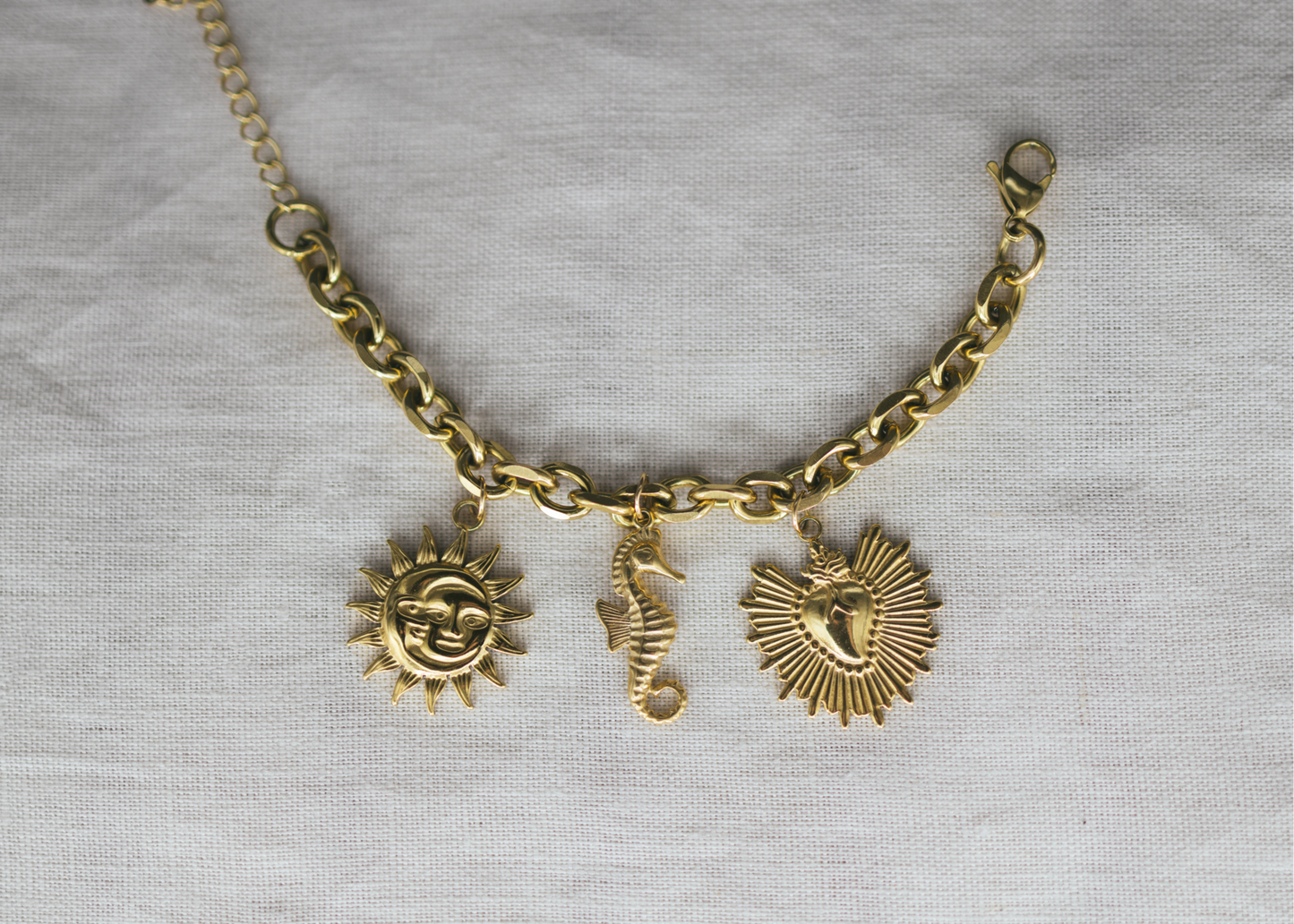 Gold Charm Beach Bracelet. Gold chain bracelet with sun and seahorse charms on a light gray background