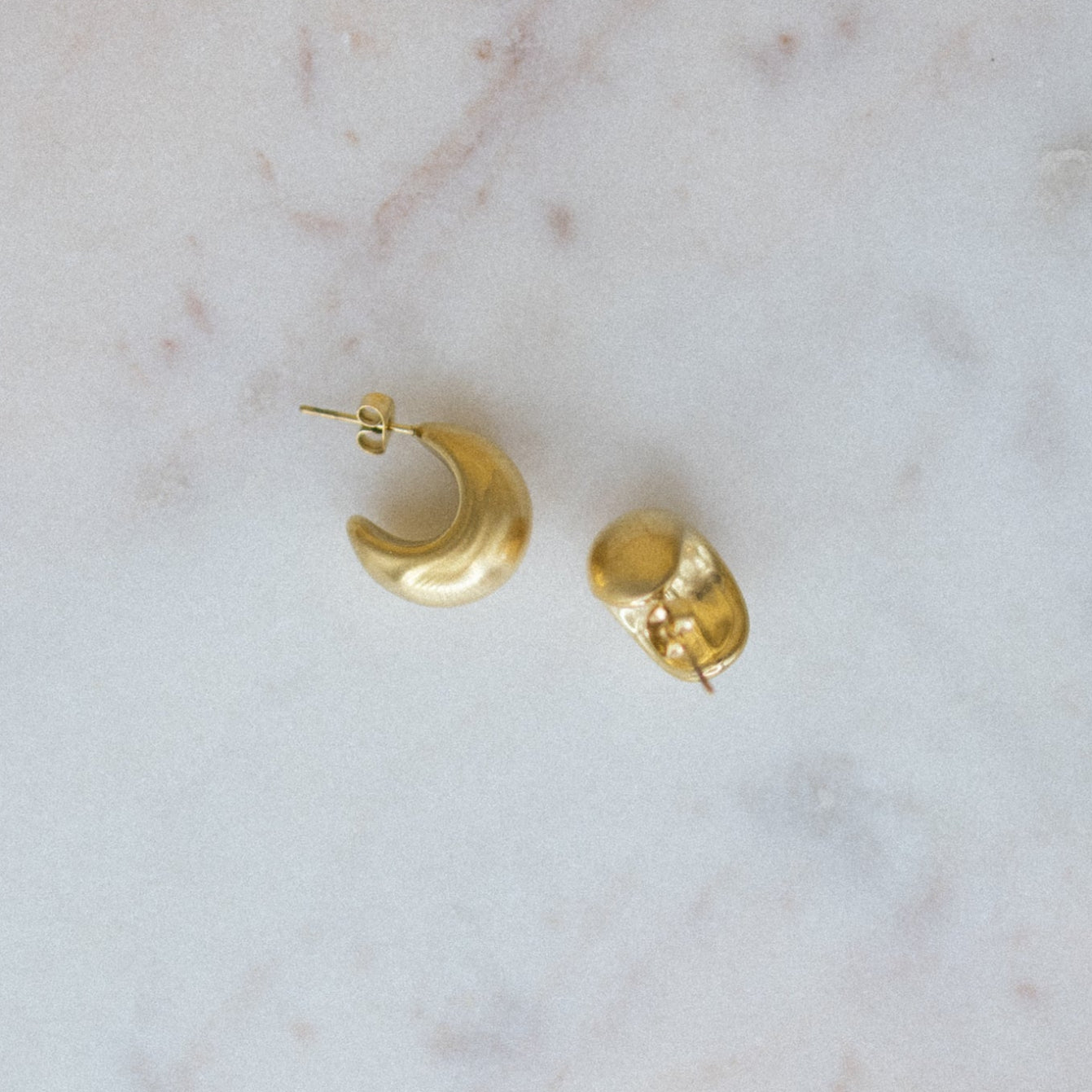 Mini Gold Textured Hoop Earrings. Two gold earrings on a marble surface