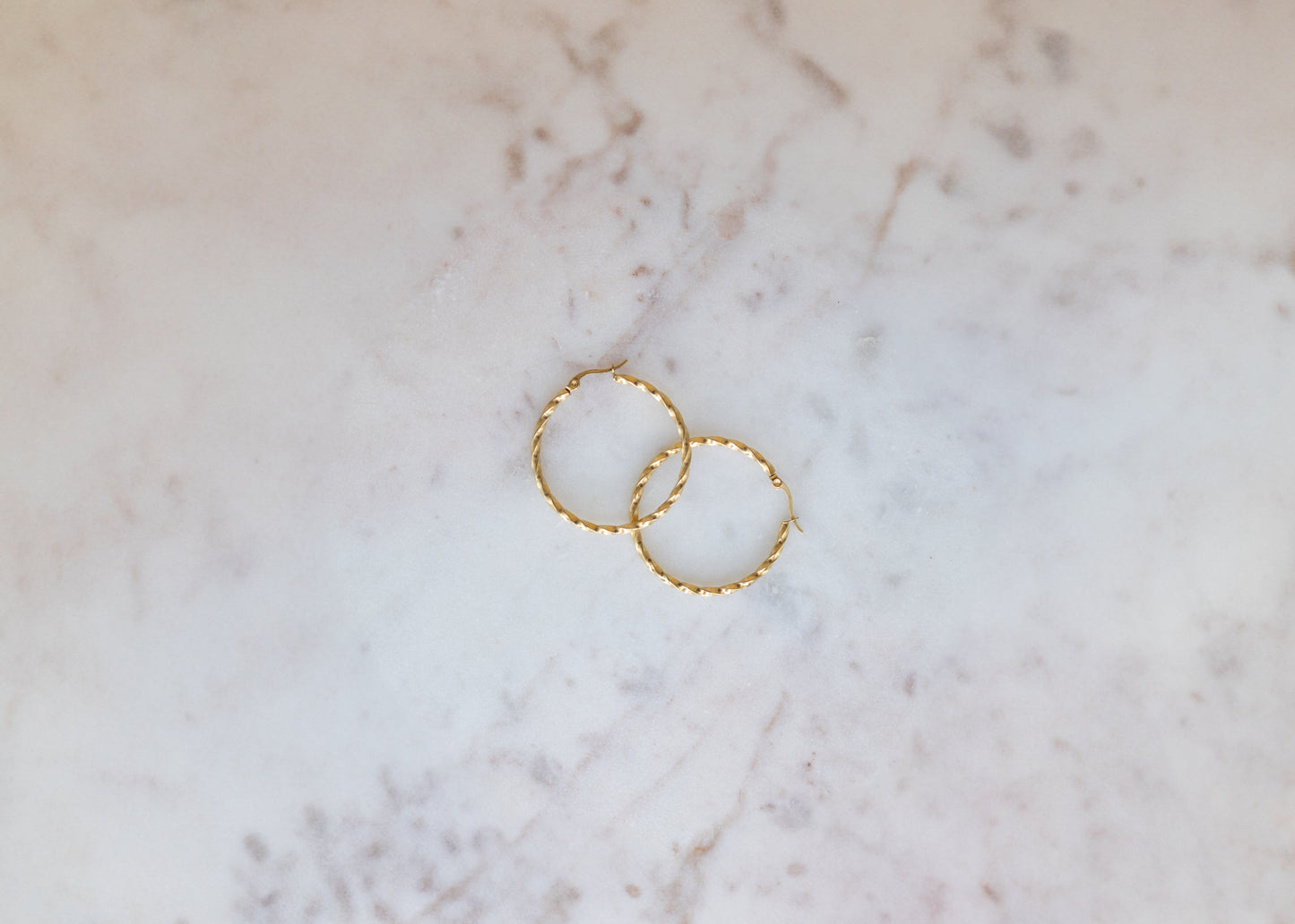 Two gold hoop earrings on a marble surface