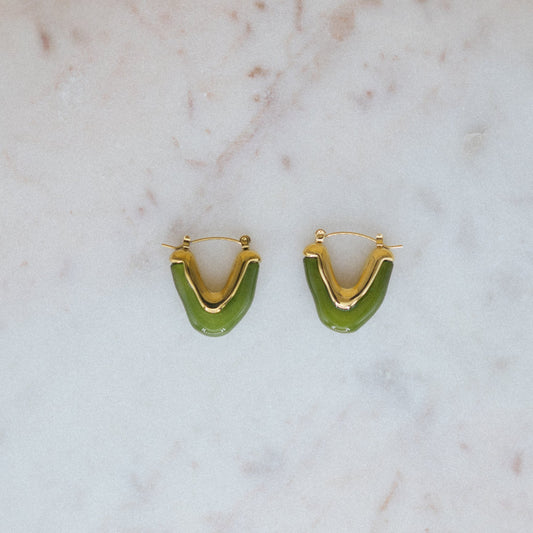 Gold hoop earrings with green crescent shapes on a marble surface