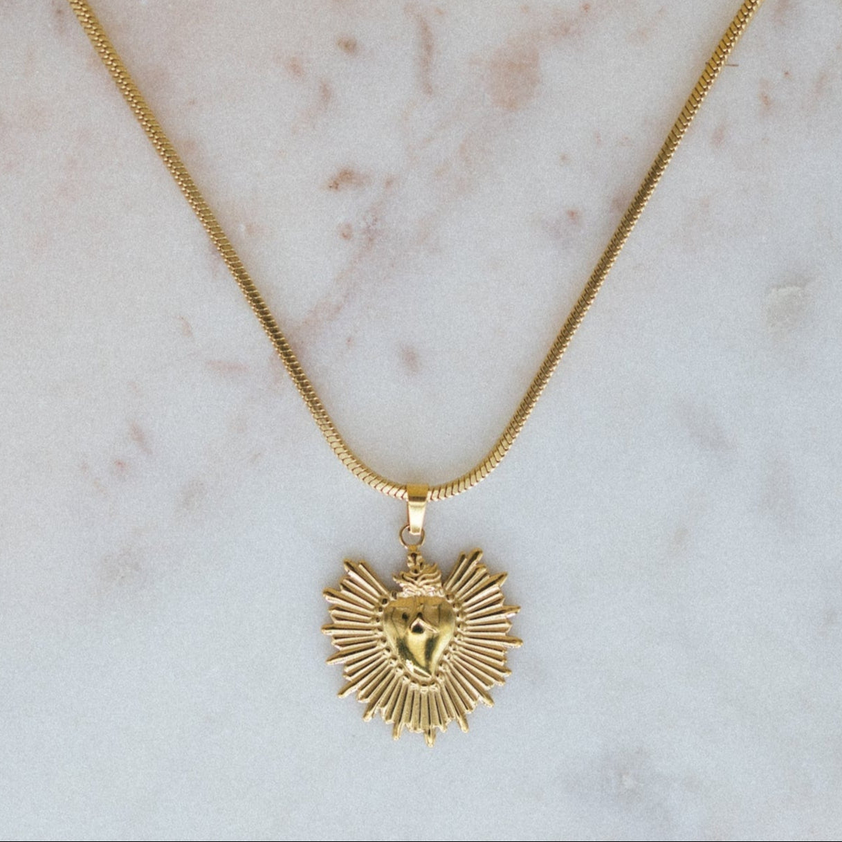 golden sunburst pendant necklace. Gold necklace with a heart-shaped pendant on a marble surface
