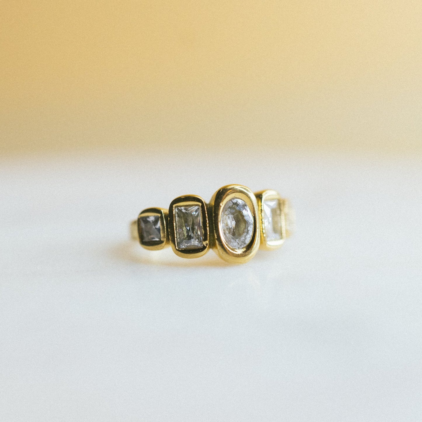 Gold ring with gemstones on a white surface with a beige background