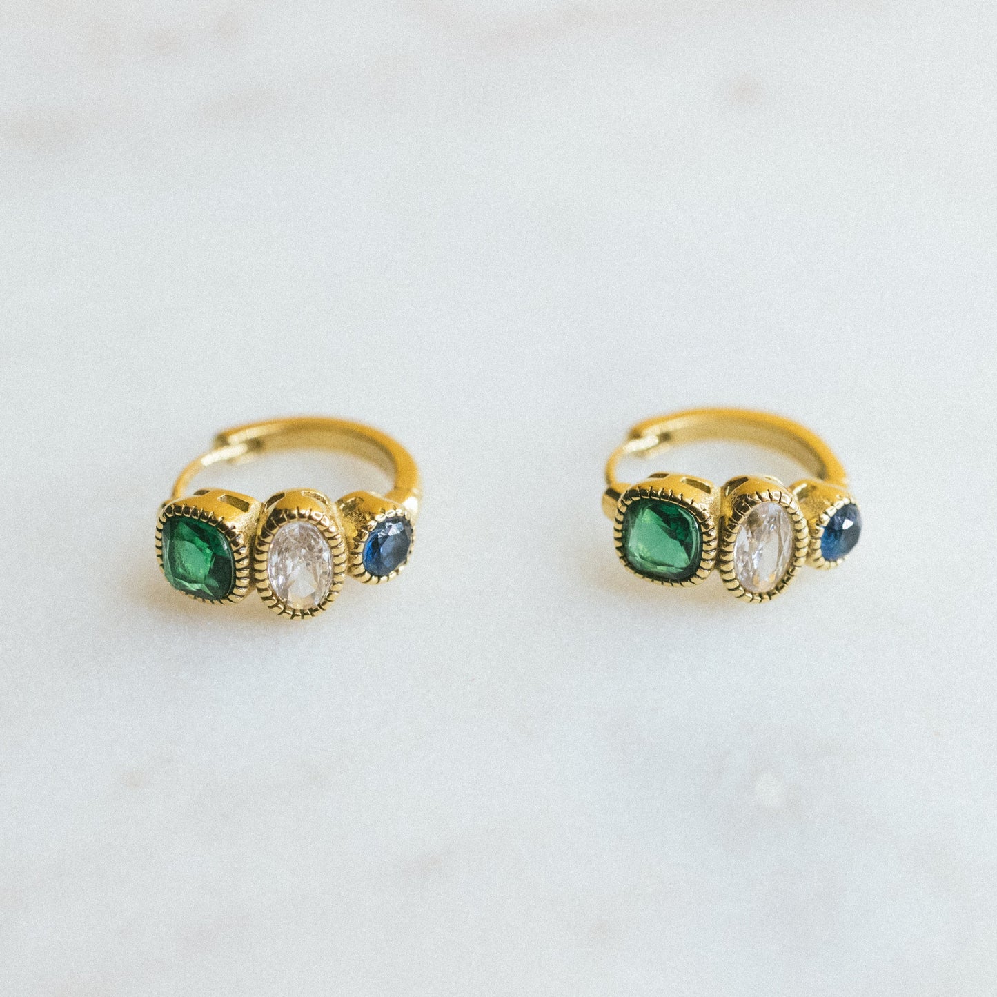 Two gold rings with green gemstones on a light gray background