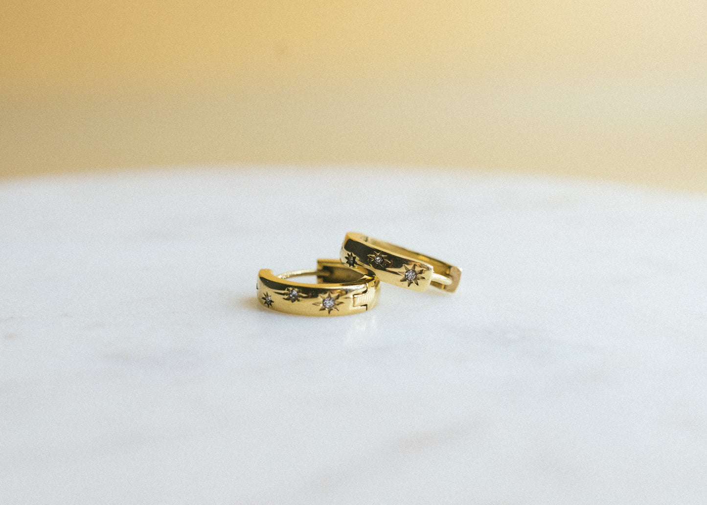 Two gold rings with intricate designs on a white surface and beige background
