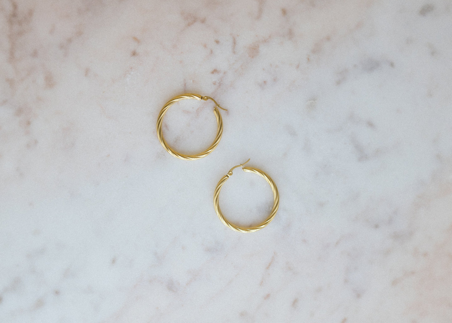 Statement Wave Hoops Earrings. Gold hoop earrings on a marble surface
