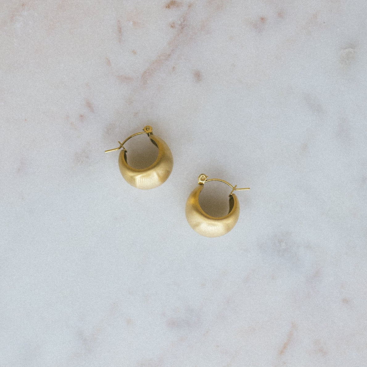 Textured Gold Crescent Hoop Earrings. Gold hoop earrings on a marble surface