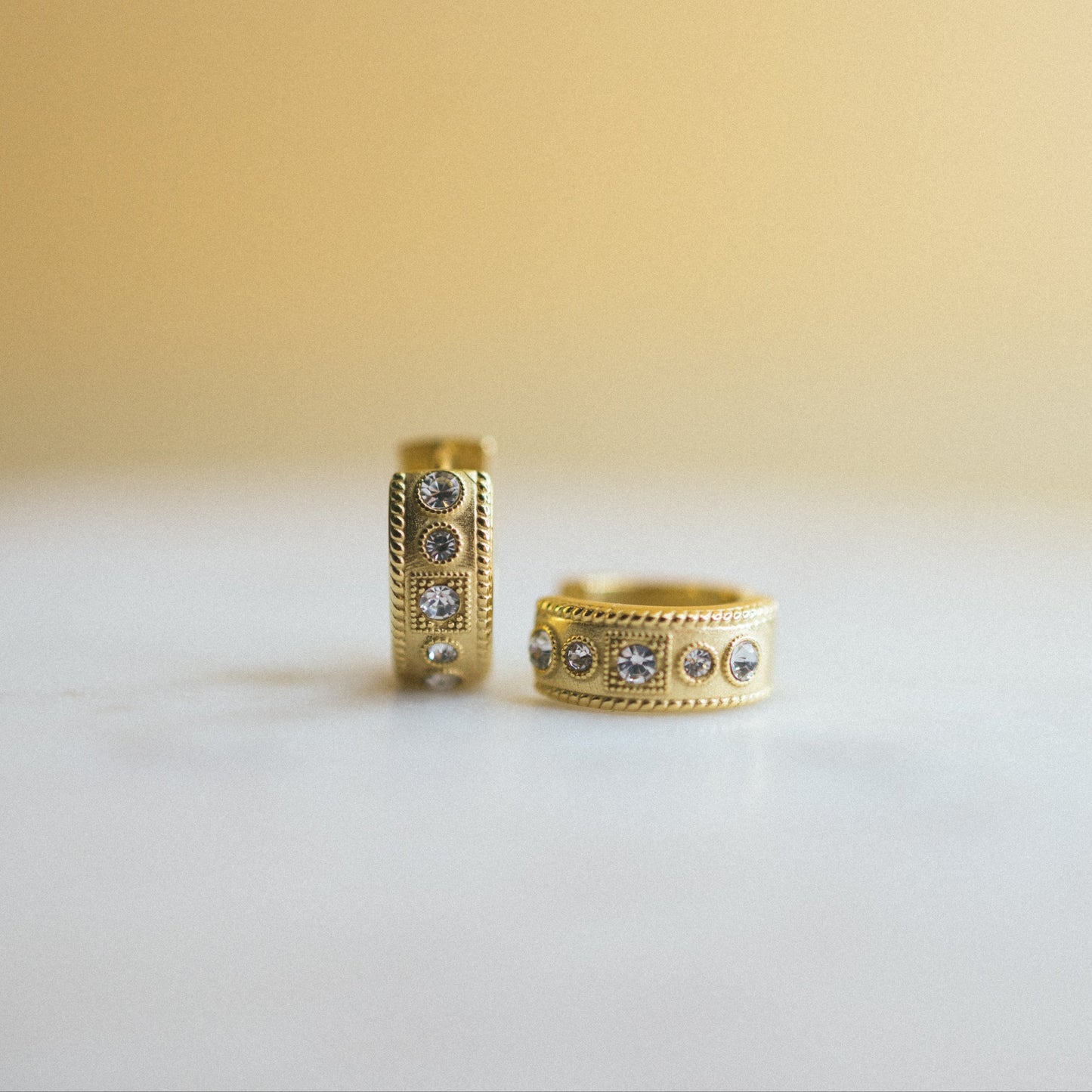 Two gold rings with gemstones on a white surface and beige background