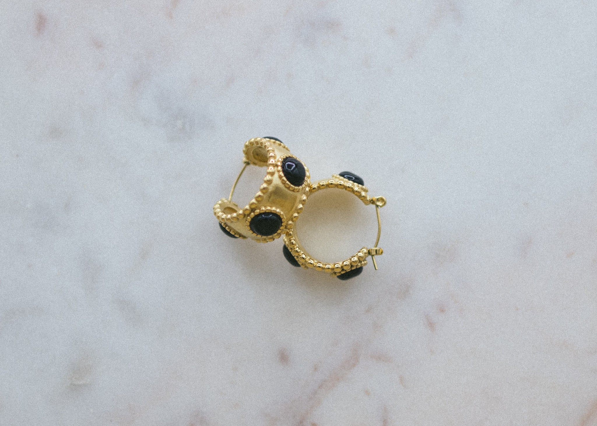 Black Grounding Gold Hoop Earrings. Gold and black earring on a marble surface