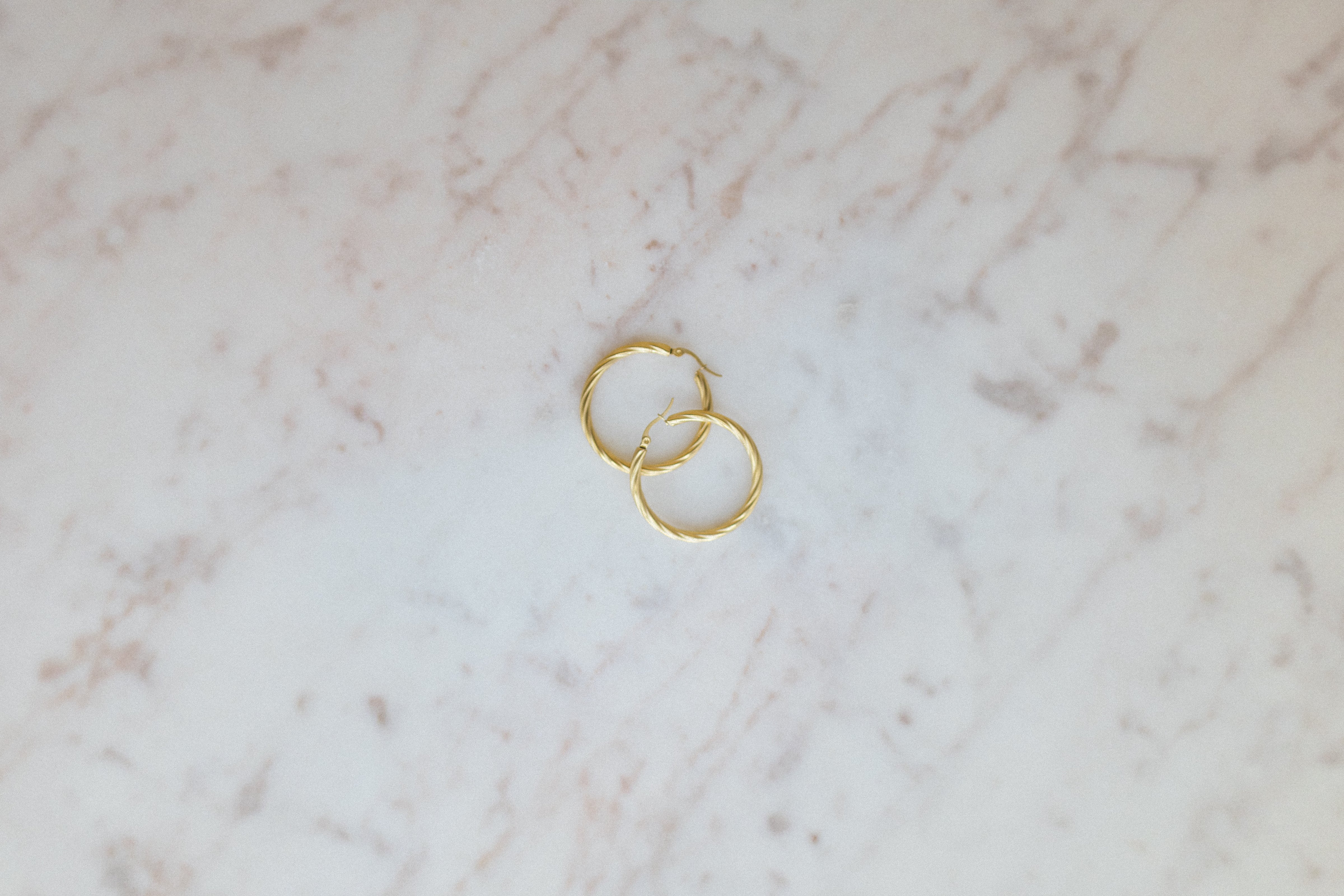 Everyday Wave Hoop Earrings. Gold hoop earrings on a marble surface