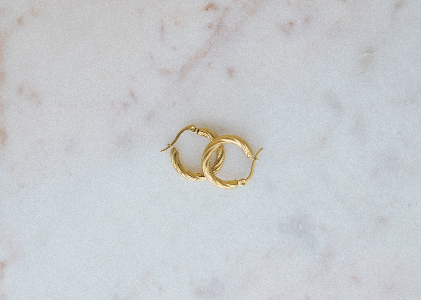 Gold-Plated Petite Glimmer Hoop Earrings. Gold hoop earrings on a marble surface