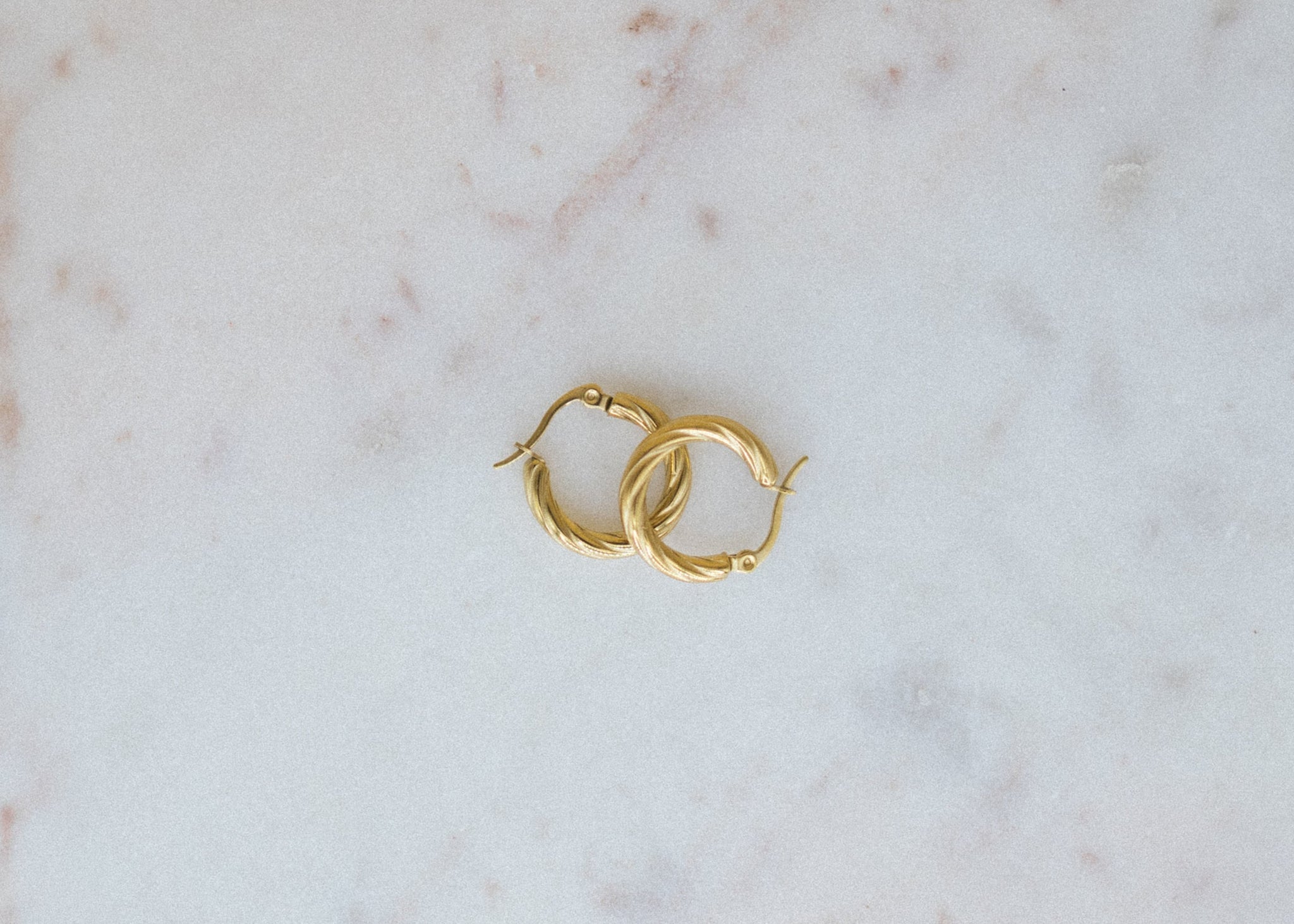 Gold-Plated Petite Glimmer Hoop Earrings. Gold hoop earrings on a marble surface