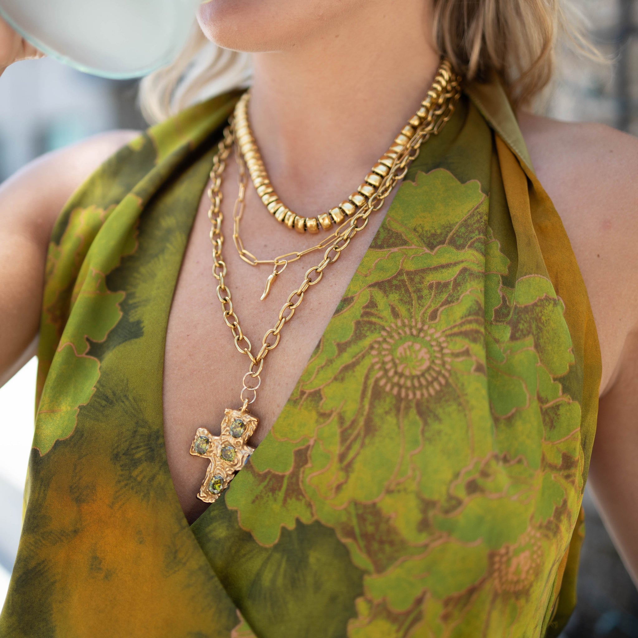 Person wearing a green patterned top with gold jewelry, including a necklace and bracelets.