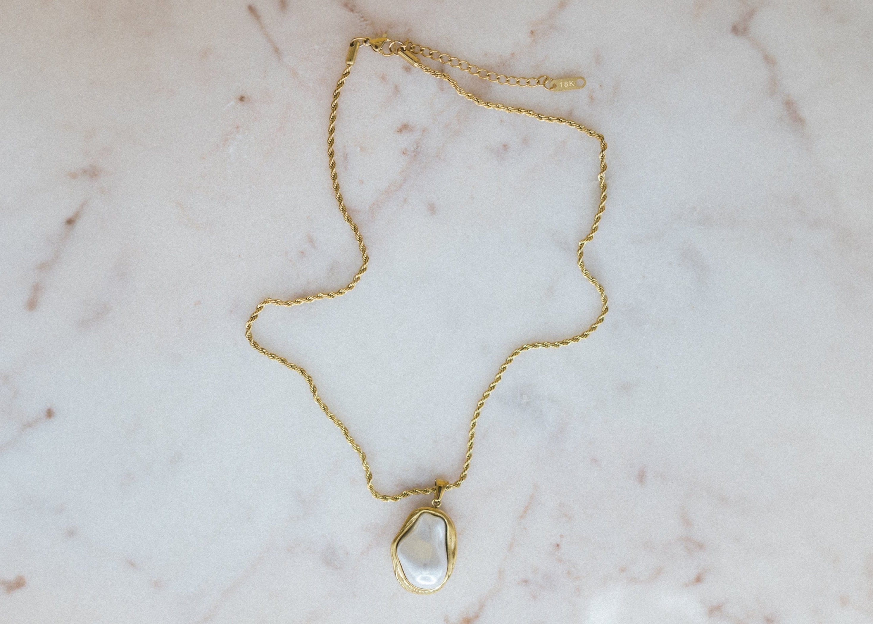 Golden Tides Necklace. Gold necklace with a teardrop-shaped pendant on a marble surface