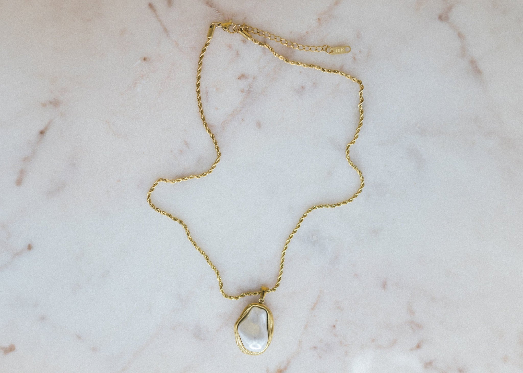 Golden Tides Necklace. Gold necklace with a teardrop-shaped pendant on a marble surface