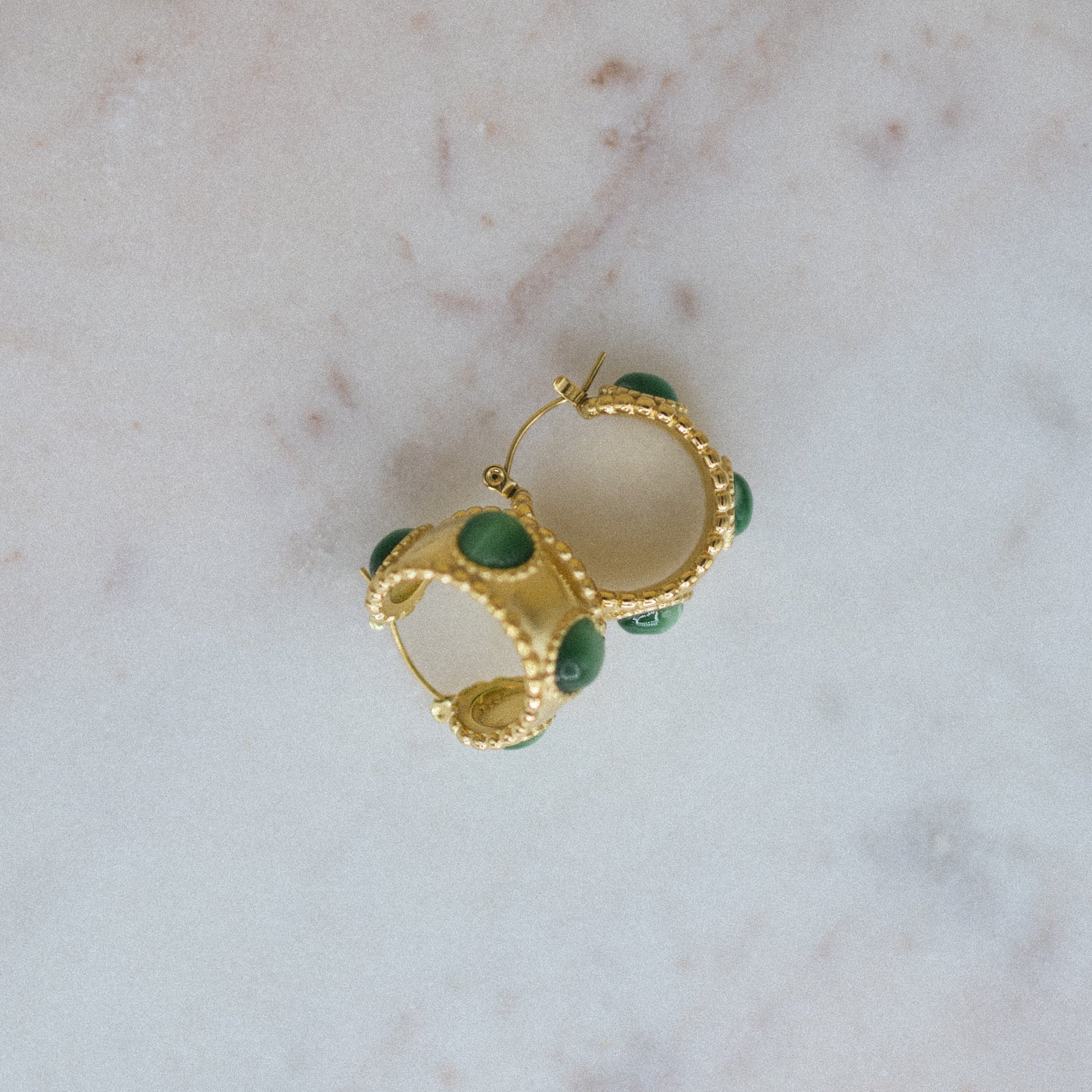 Gold hoop earrings with green stones on a marble surface