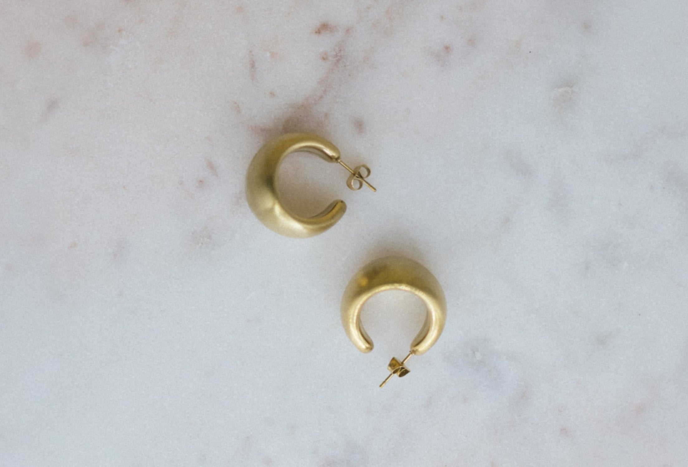 Mini Gold Textured Hoop Earrings. Gold hoop earrings on a marble surface