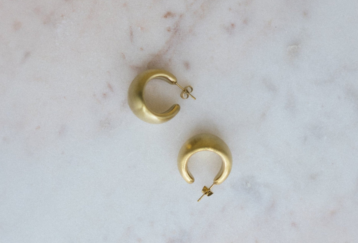 Mini Gold Textured Hoop Earrings. Gold hoop earrings on a marble surface