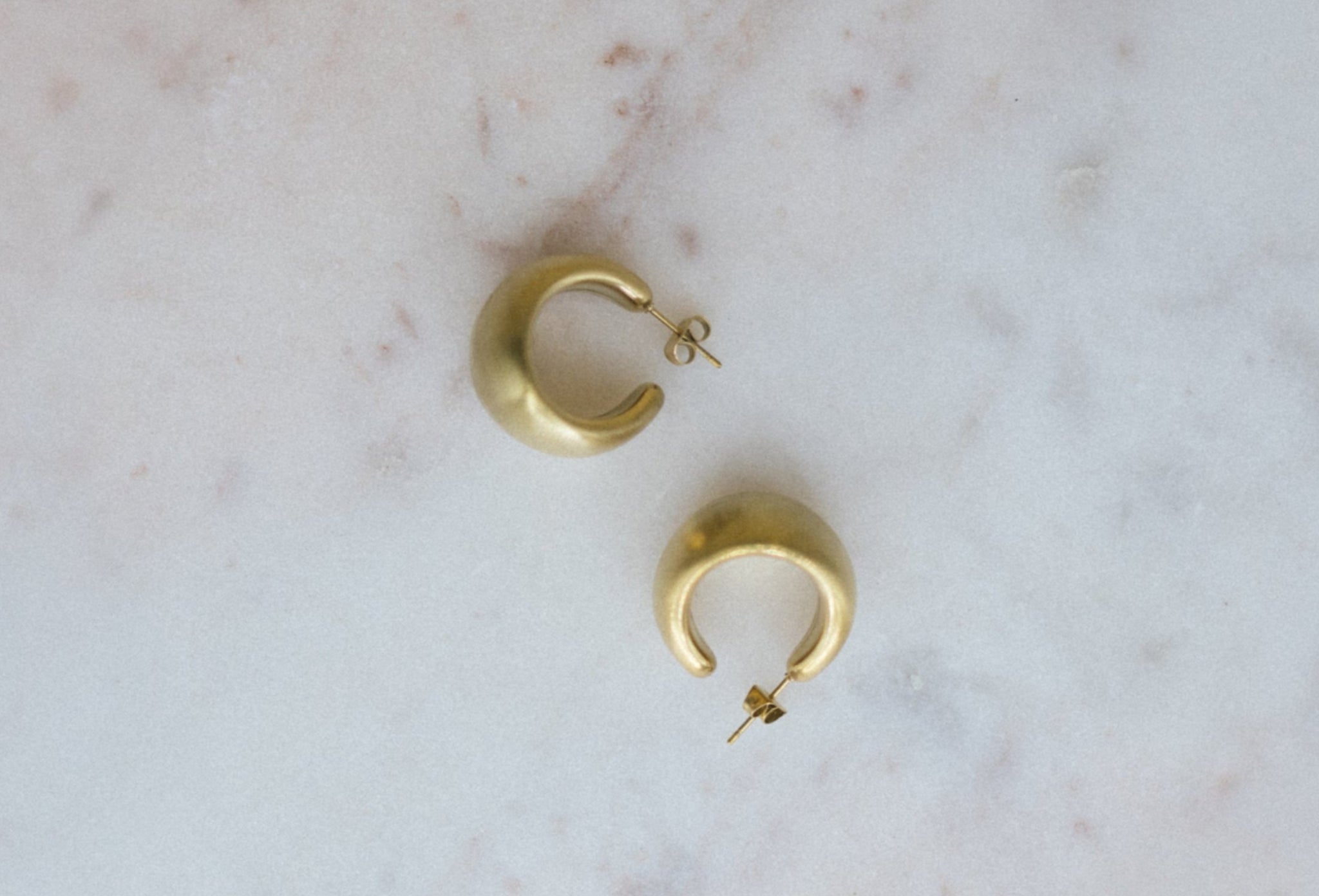 Mini Gold Textured Hoop Earrings. Gold hoop earrings on a marble surface