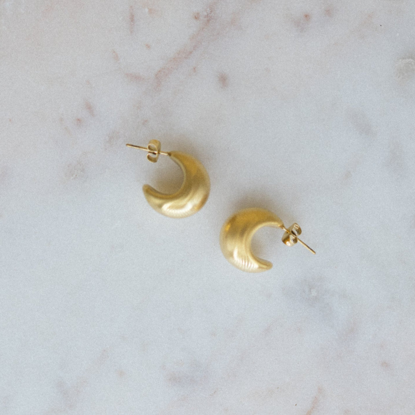 Gold crescent moon earrings on a marble surface