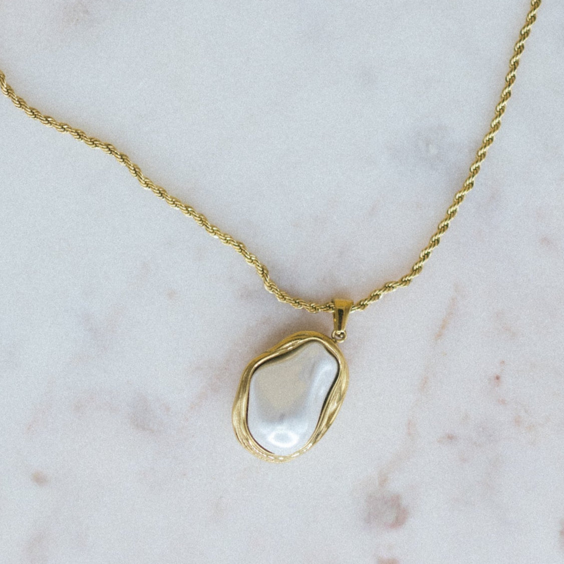 Gold necklace with a large pearl pendant on a marble background