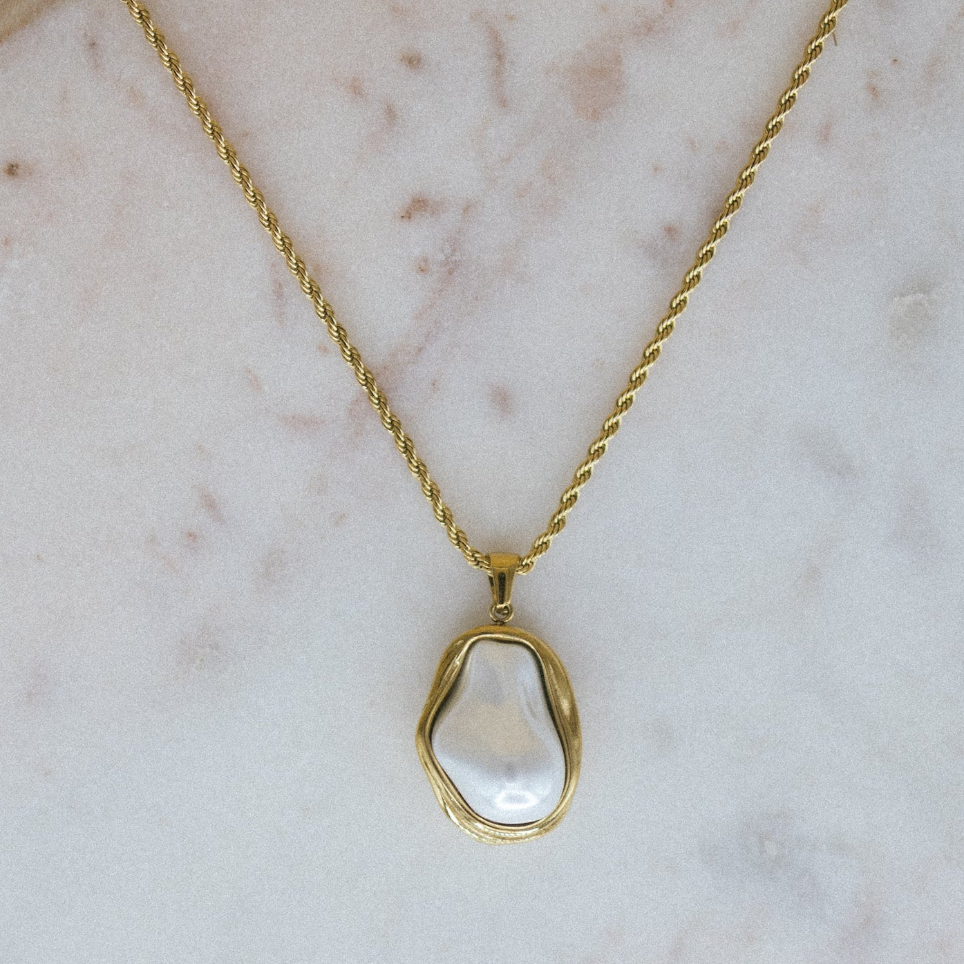 Gold necklace with a clear pendant on a marble surface