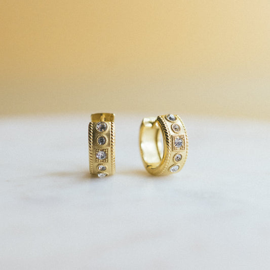 Two gold hoop earrings with embedded stones on a white surface.