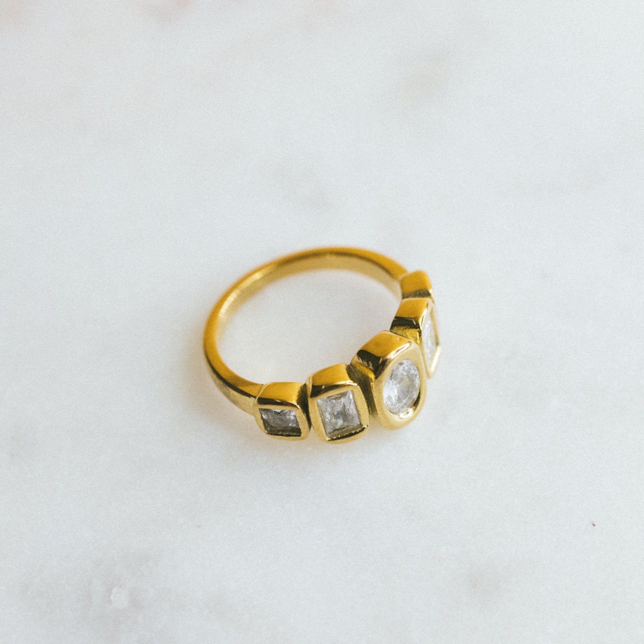 Gold ring with embedded stones on a light marble background