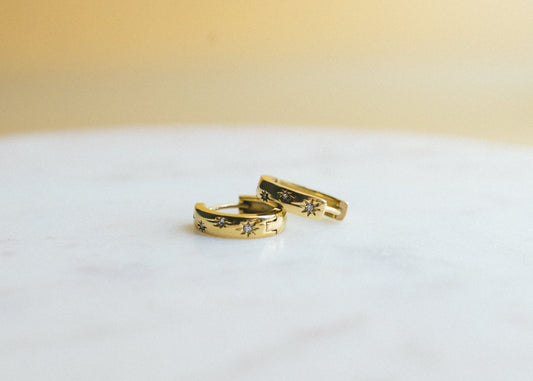 Two gold rings with intricate designs on a white surface and beige background