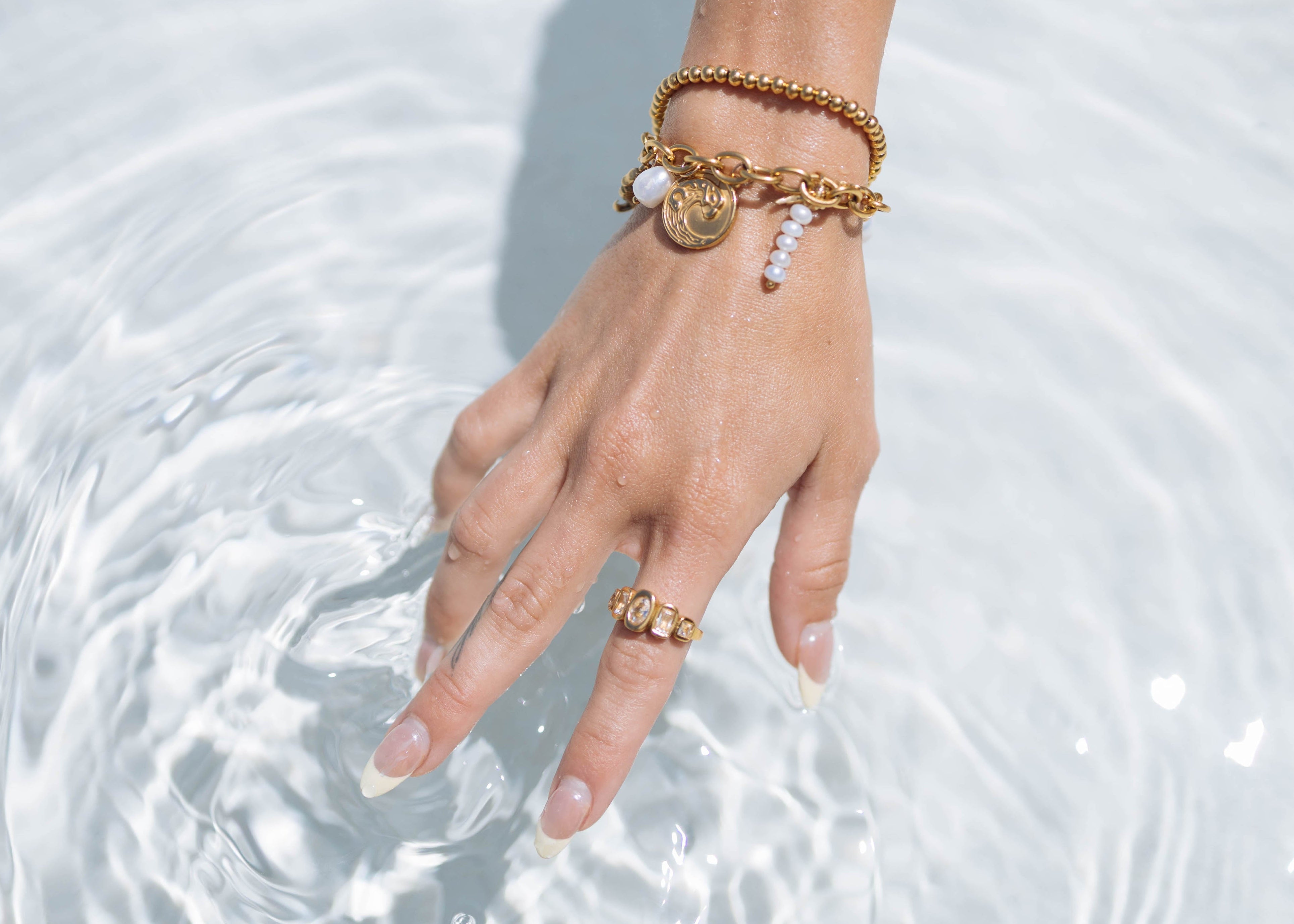 Hand with gold bracelets and ring touching water