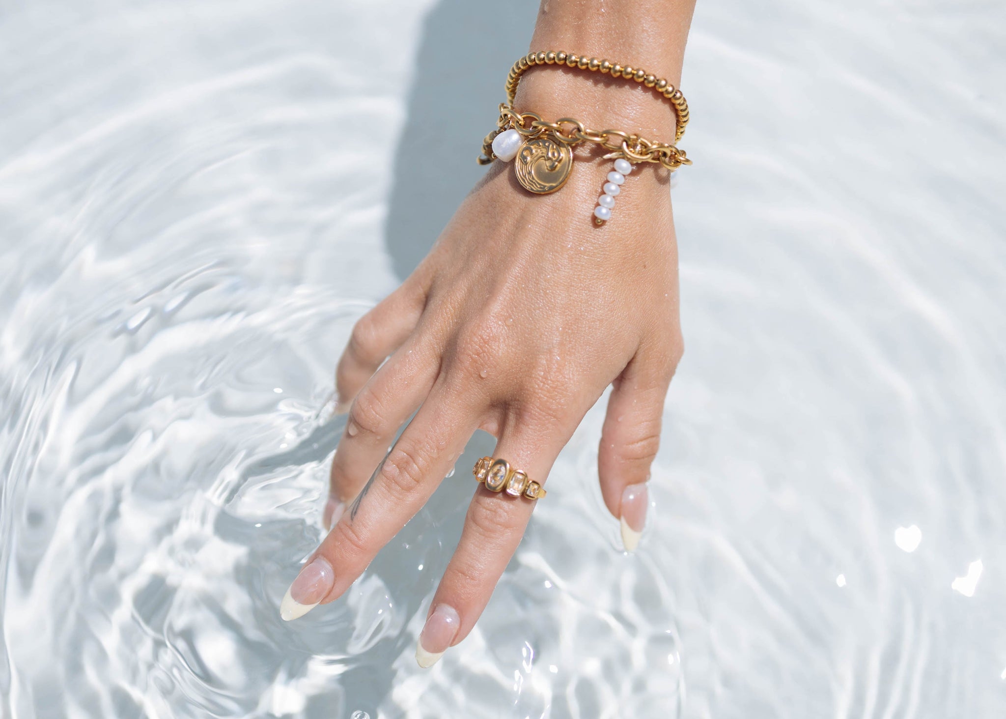 Hand with gold bracelets and ring touching water