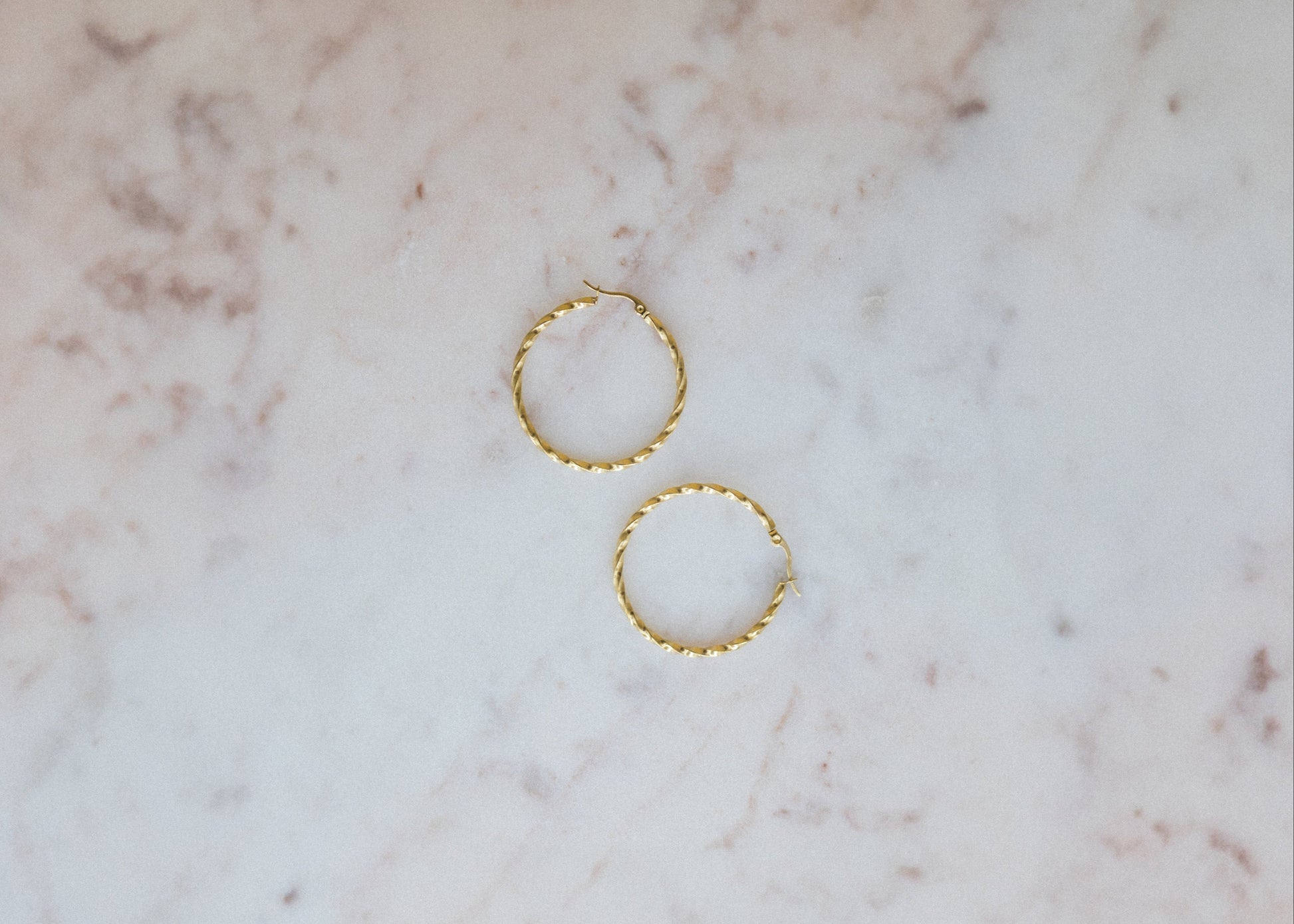 Statement Twist Hoop Earrings. Two gold hoop earrings on a marble surface
