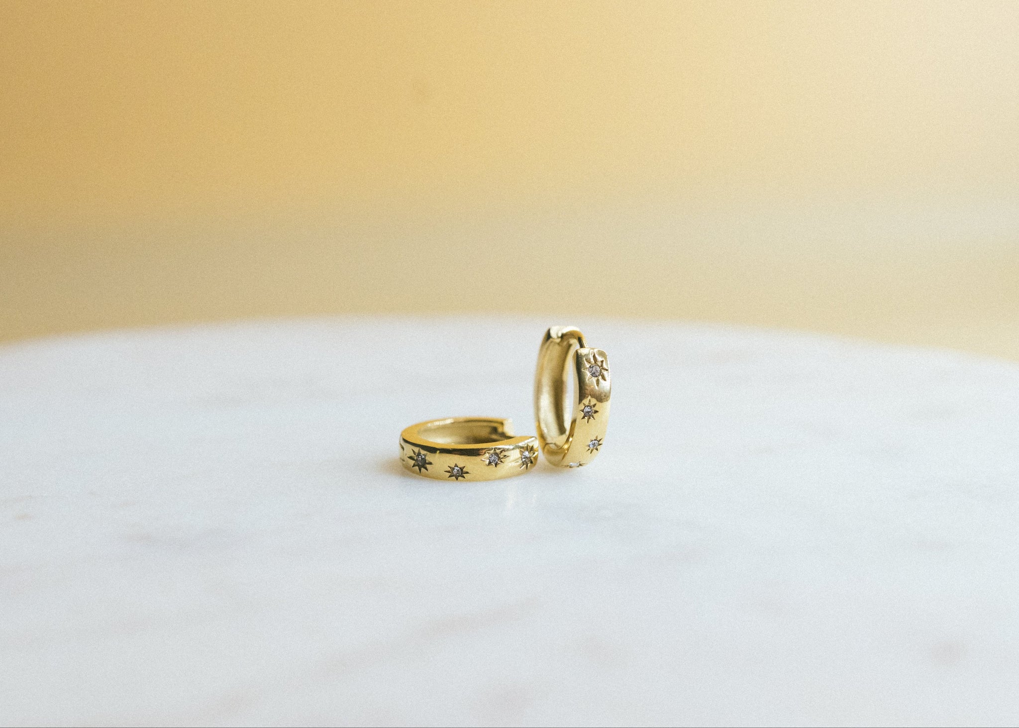Sunbeam Glow Huggies. Two gold rings on a white surface with a beige background