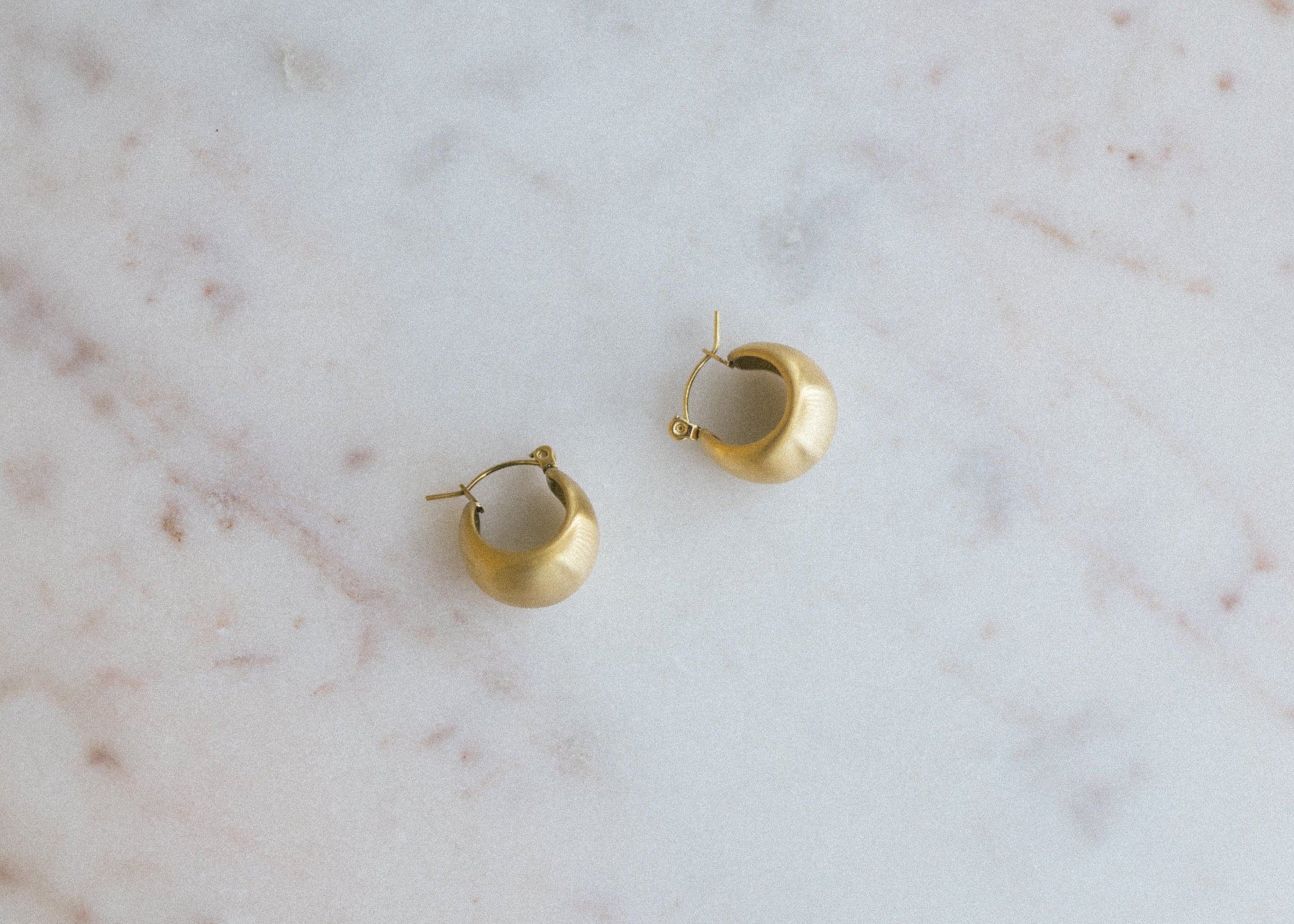 Textured Gold Crescent Hoop Earrings. Gold hoop earrings on a marble surface
