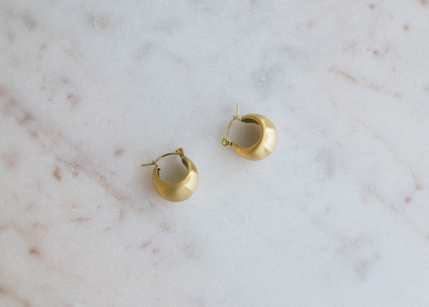 Textured Gold Crescent Hoop Earrings. Gold hoop earrings on a marble surface