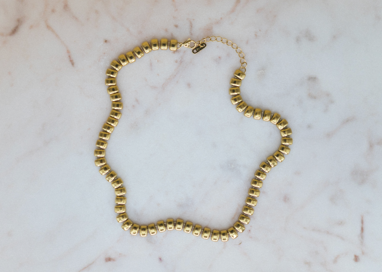 The Golden Bead Chain Necklace. Gold beaded necklace on a marble surface