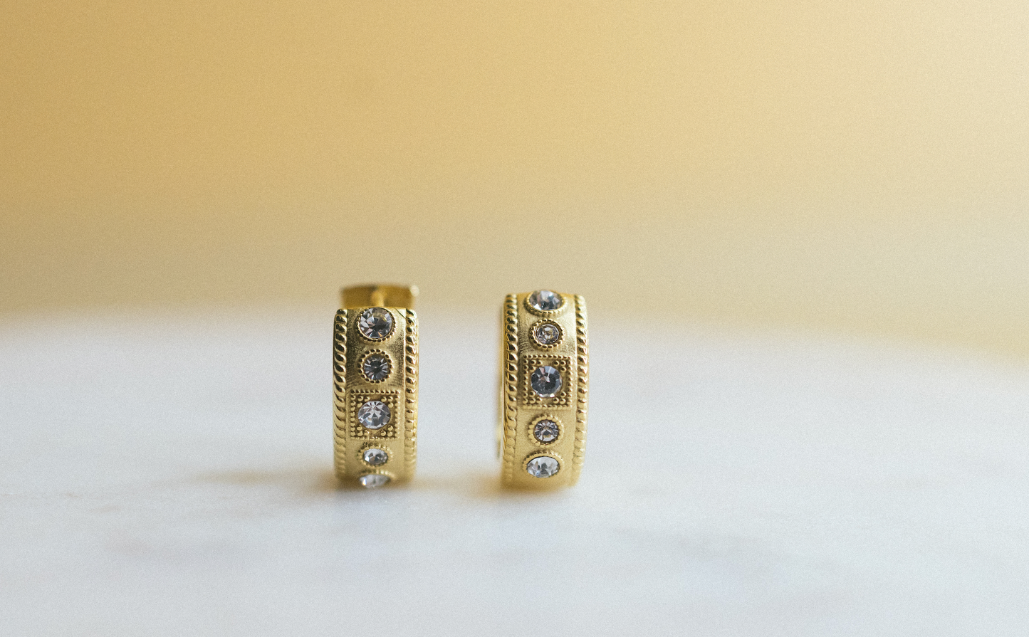 gold edge huggie earrings. Gold hoop earrings with embedded stones on a light background