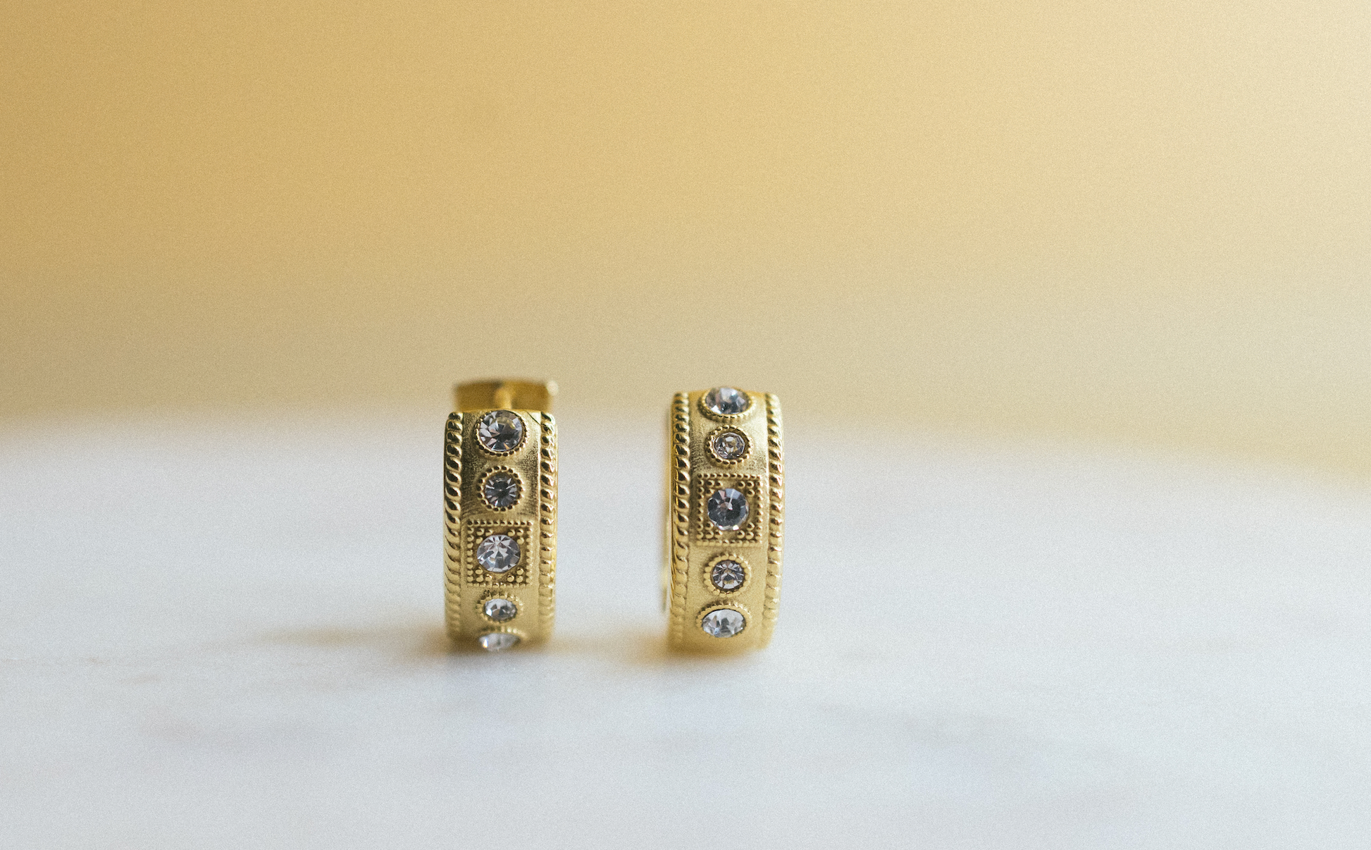 gold edge huggie earrings. Gold hoop earrings with embedded stones on a light background