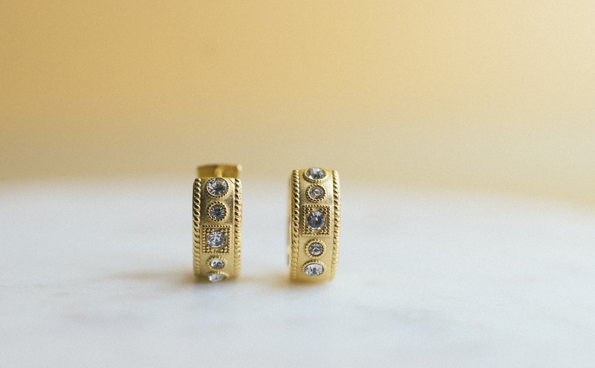 gold edge huggie earrings. Gold hoop earrings with embedded stones on a light background
