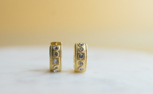 gold edge huggie earrings. Gold hoop earrings with embedded stones on a light background