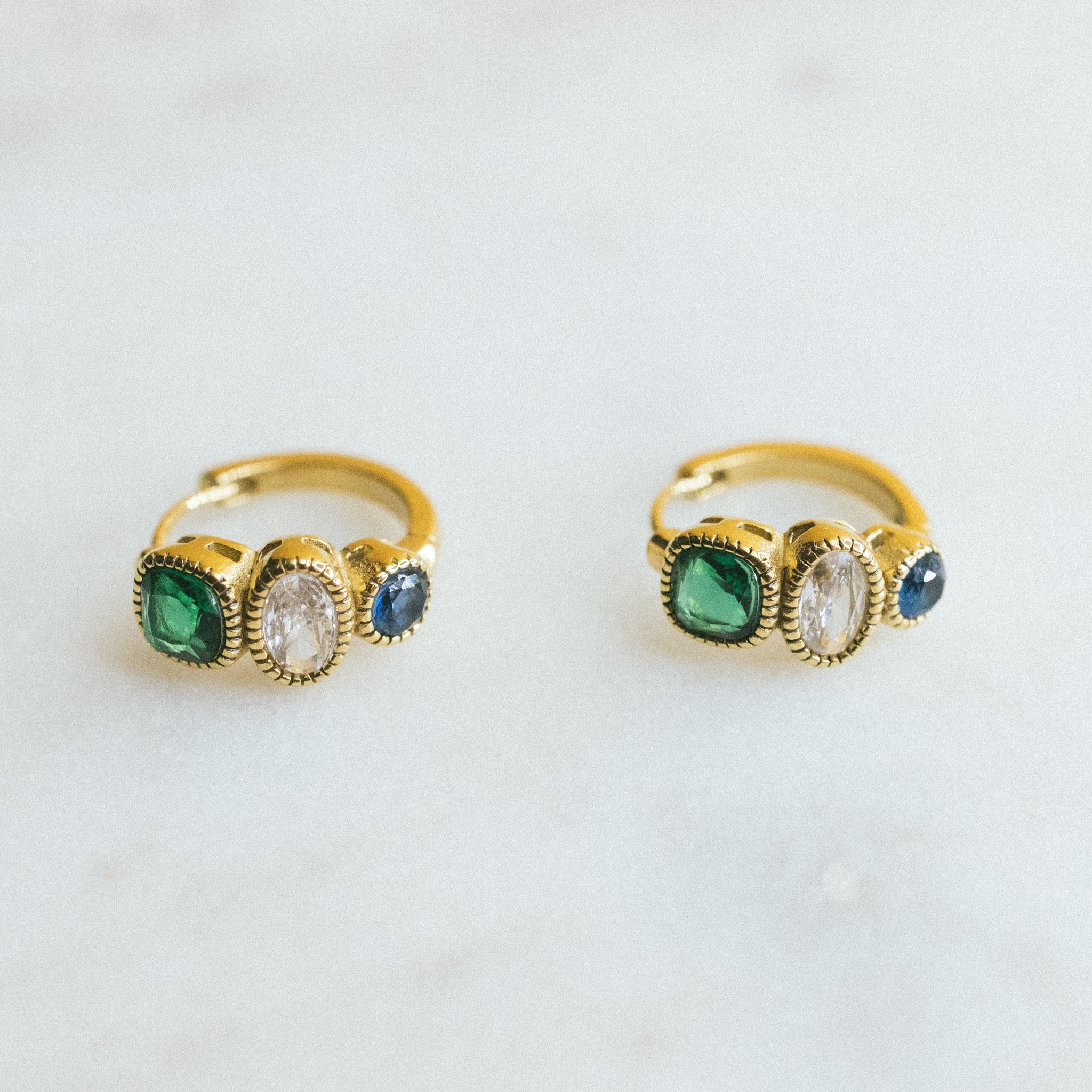 Two gold rings with green gemstones on a light gray background