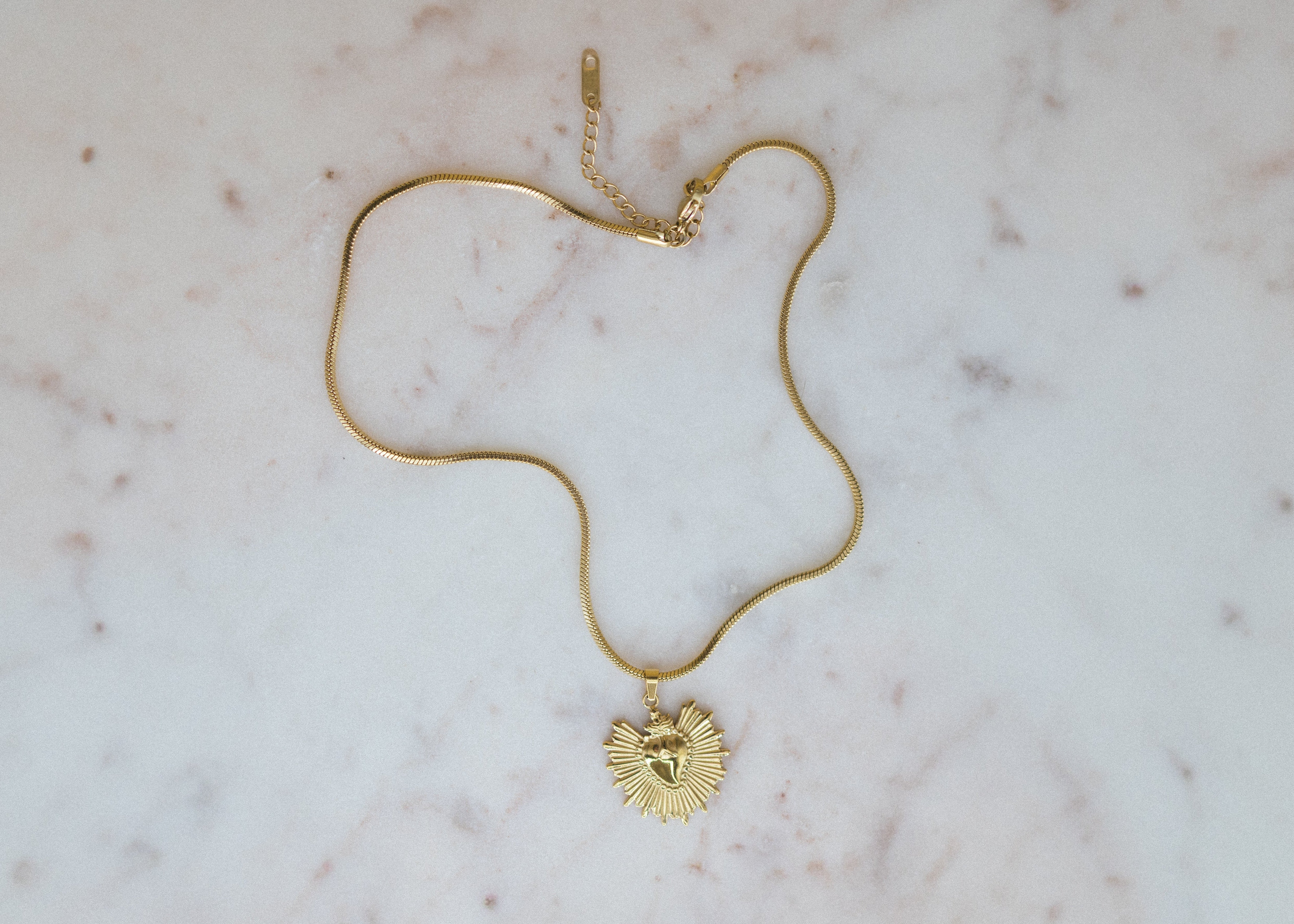 golden sunburst pendant necklace. Gold necklace with a heart pendant on a marble surface