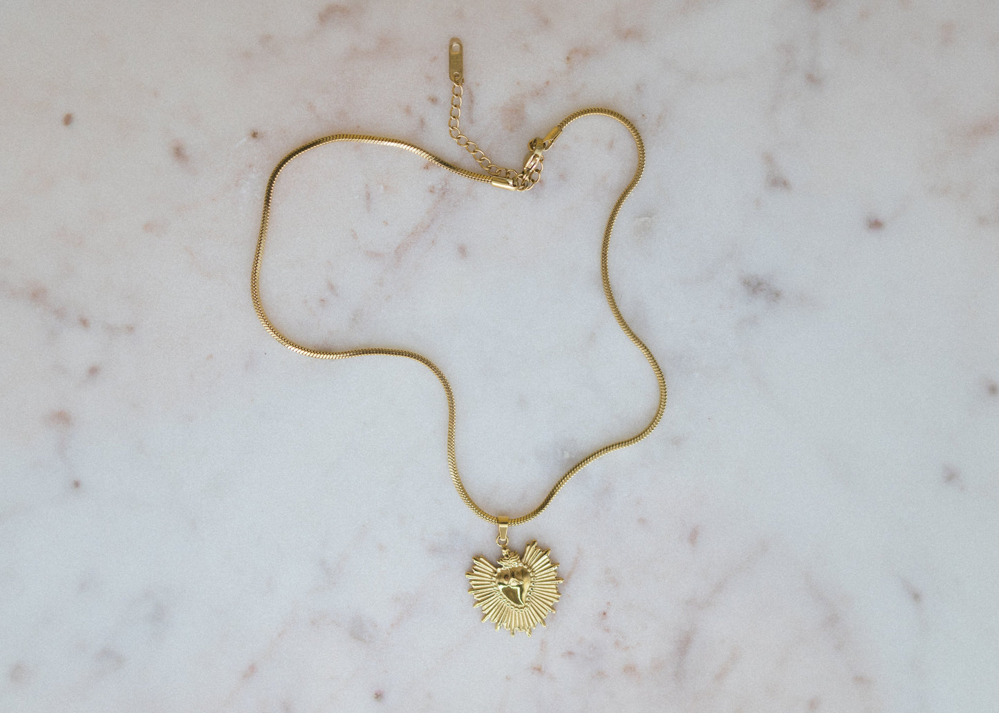 golden sunburst pendant necklace. Gold necklace with a heart pendant on a marble surface