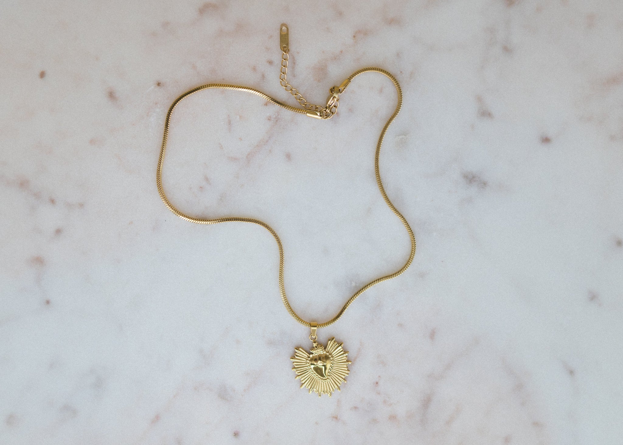 golden sunburst pendant necklace. Gold necklace with a heart pendant on a marble surface