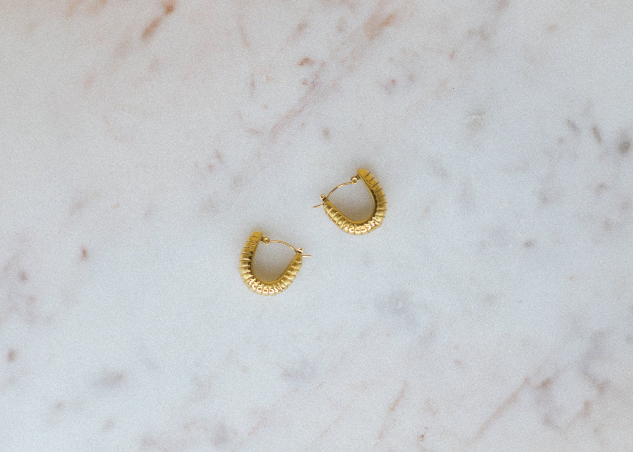 the classic u. Gold hoop earrings on a marble surface