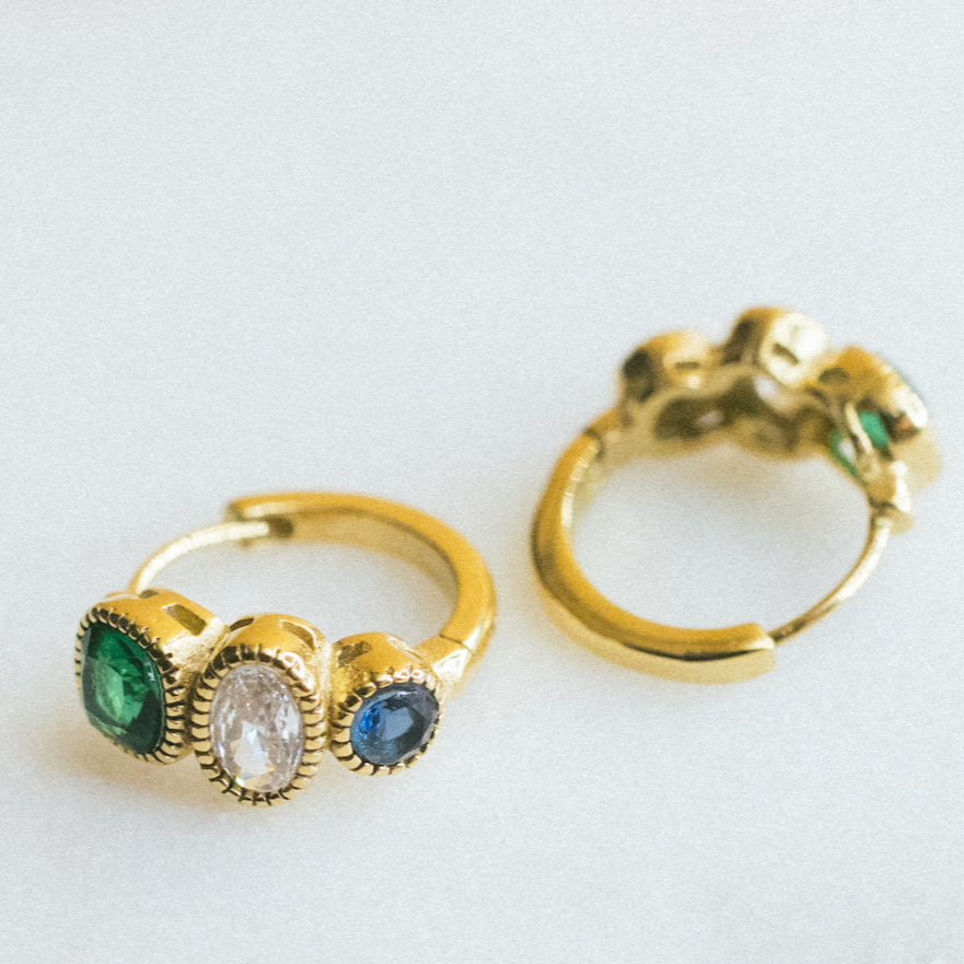 Two gold huggies earrings with gemstones on a light gray background